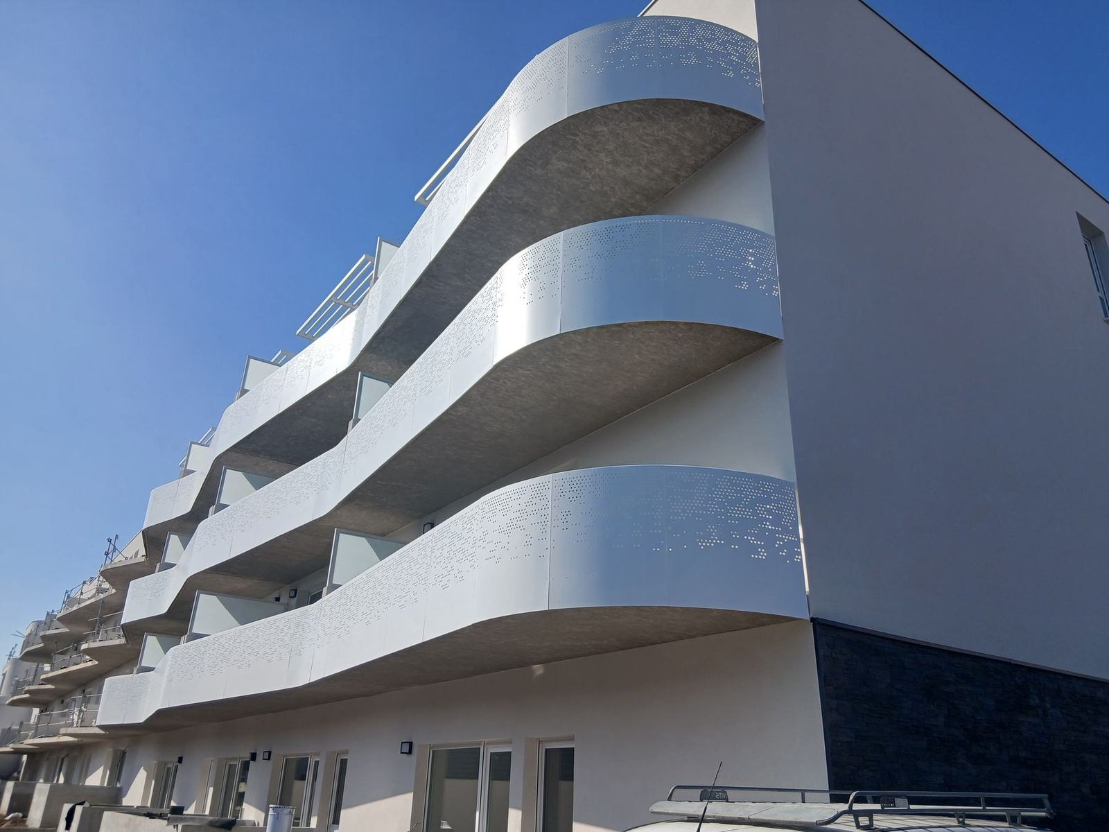 Façade d'un immeuble neuf aux balcons courbes, sous un ciel bleu